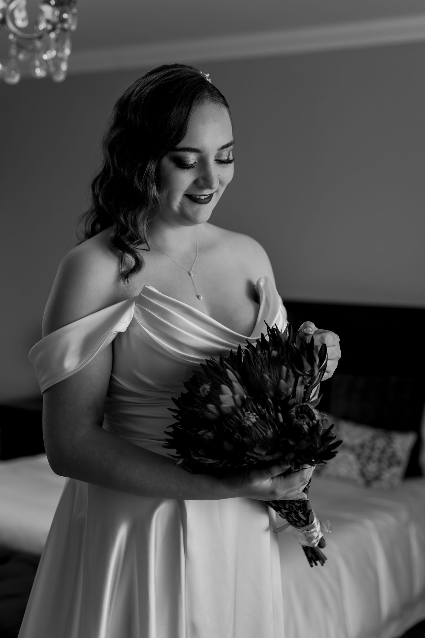 Black and white portrait of bride in off-shoulder gown holding feathered bouquet.