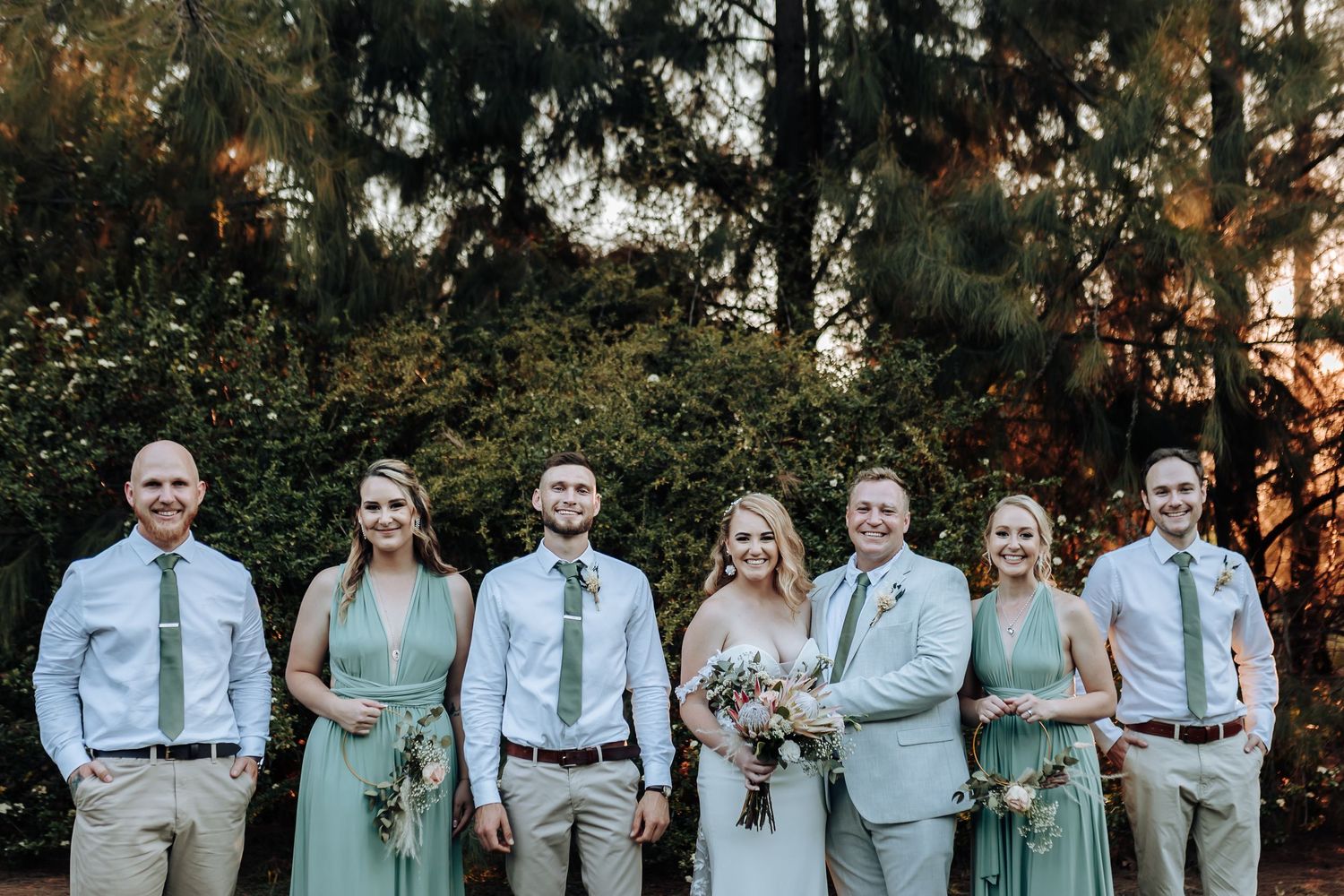 Bridal party in mint bridesmaid dresses and light gray suits posed for formal photo.