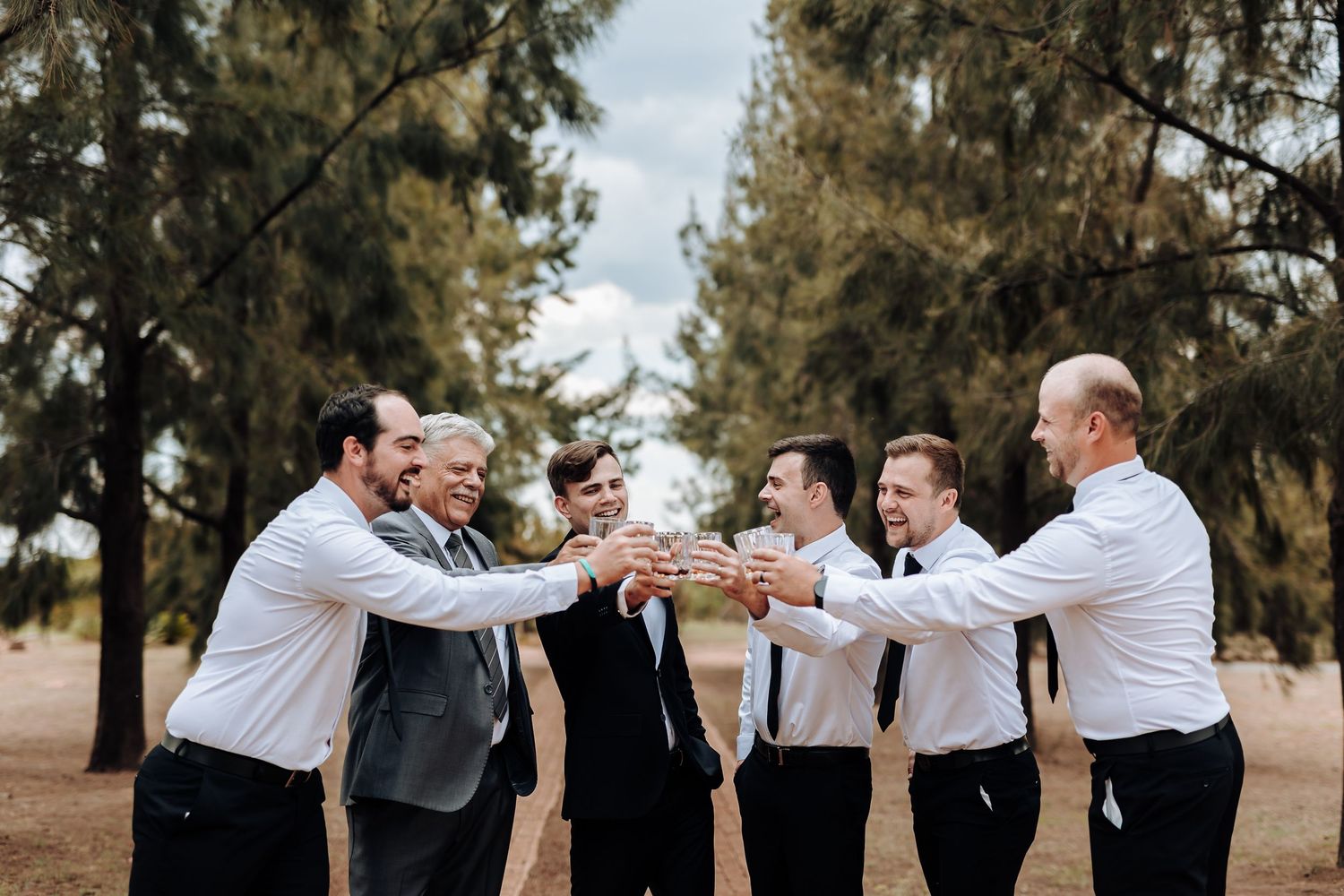 Groomsmen celebrate with animated gestures in a circle formation outdoors.