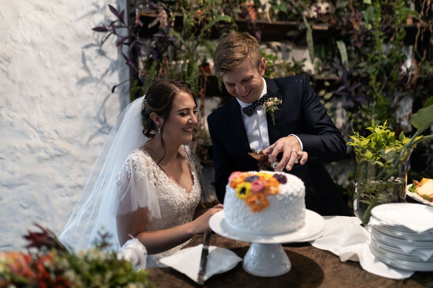 Newlyweds cutting into their elegant white wedding cake decorated with citrus flowers.