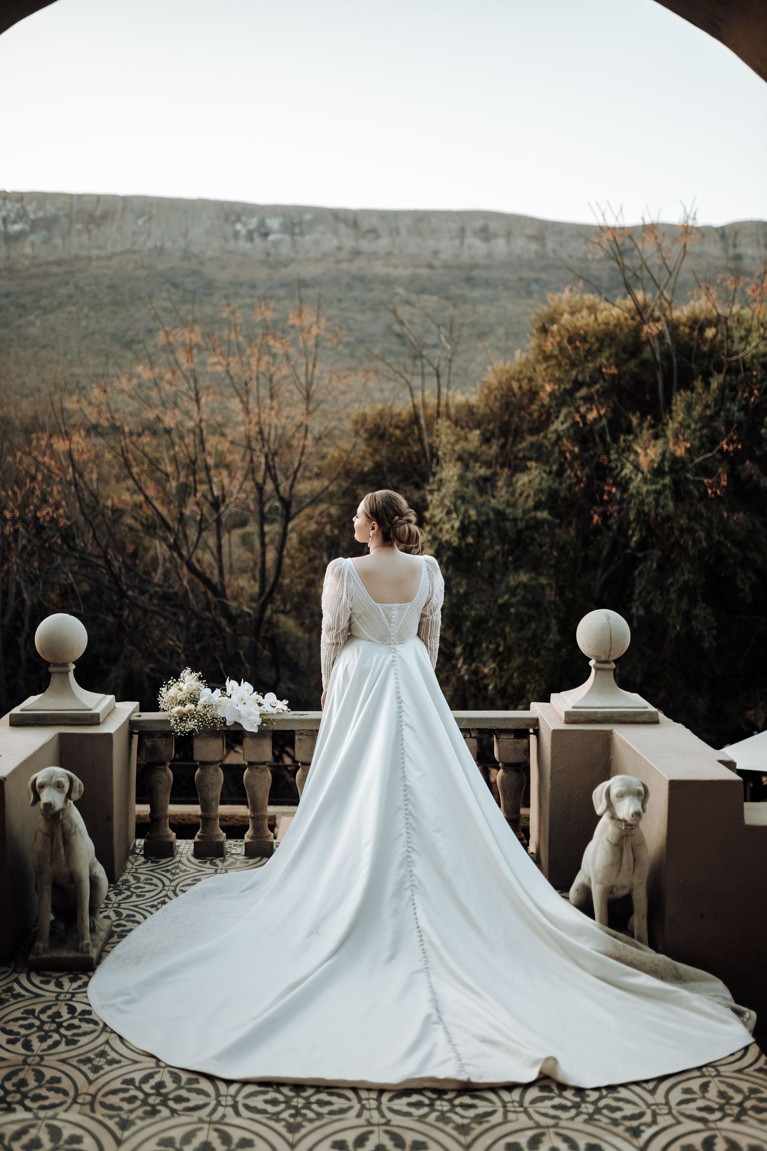 Wedding dress with long train photographed on terrace with mountain vista.