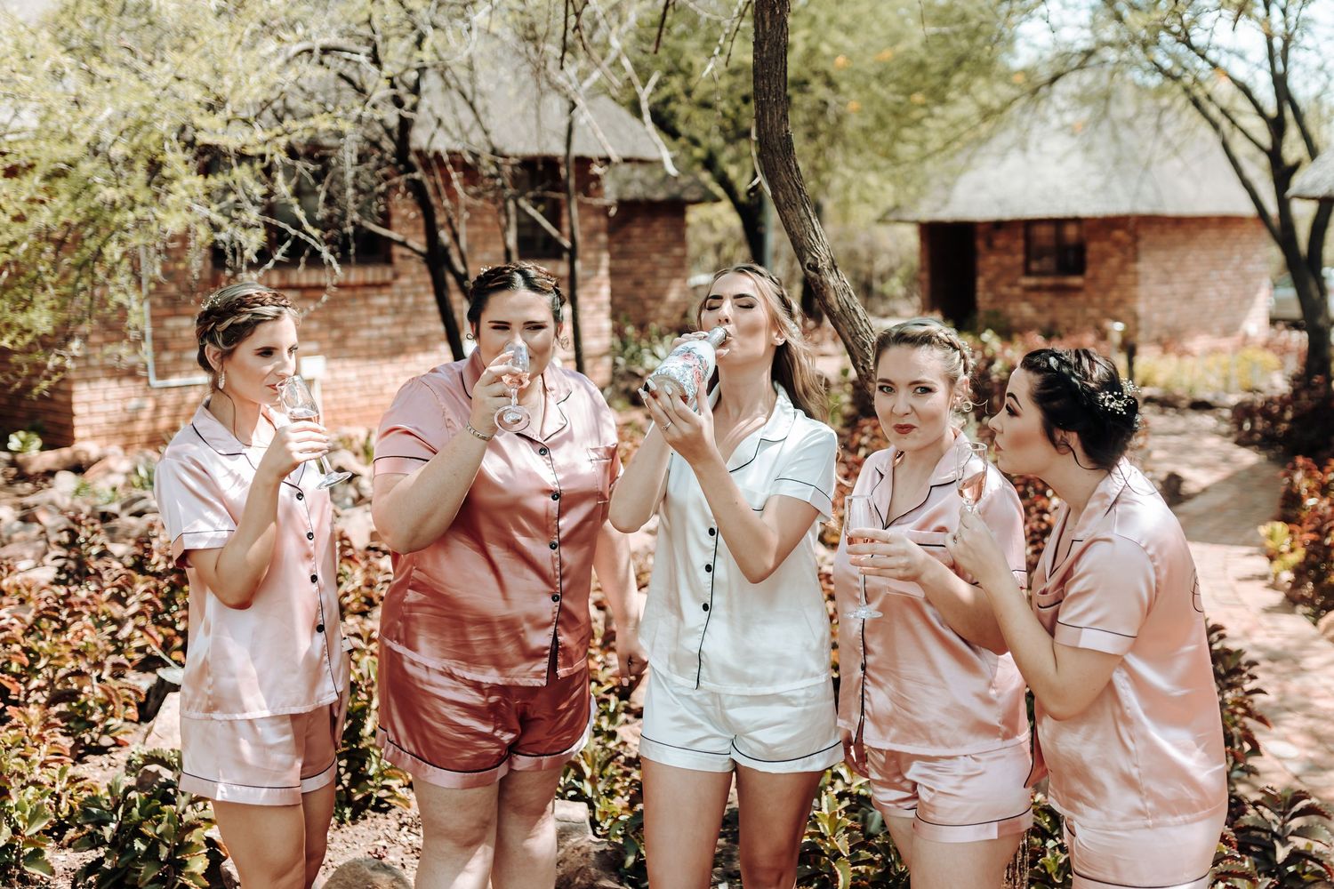 Friends in matching pajamas celebrate with champagne in an outdoor garden setting.