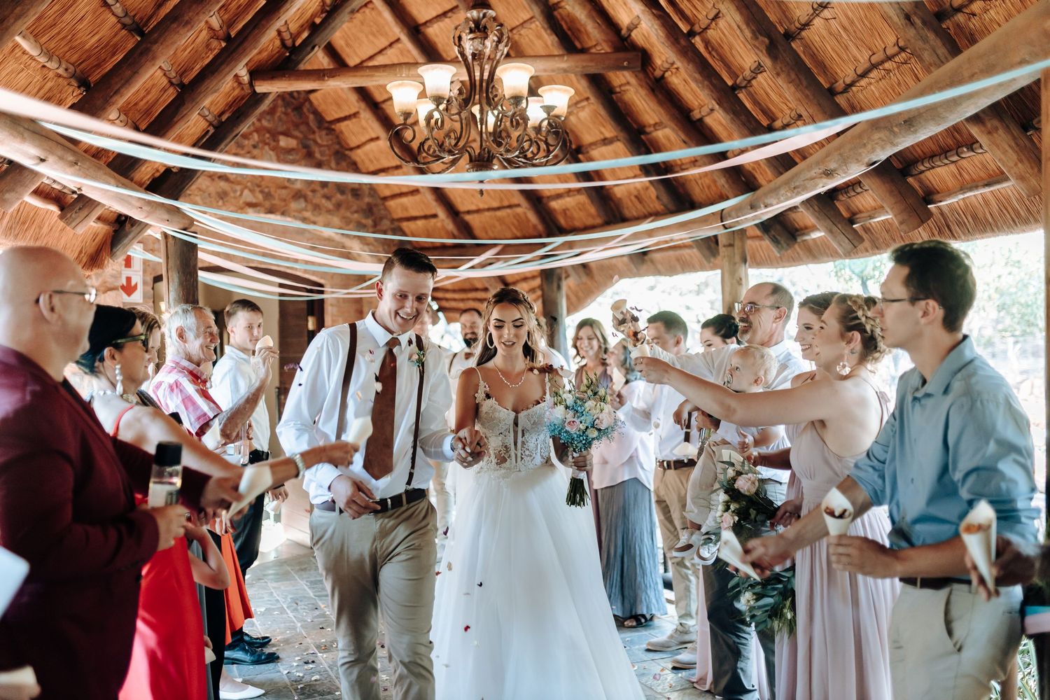 Wedding celebration under wooden beams with guests throwing confetti at the happy couple.