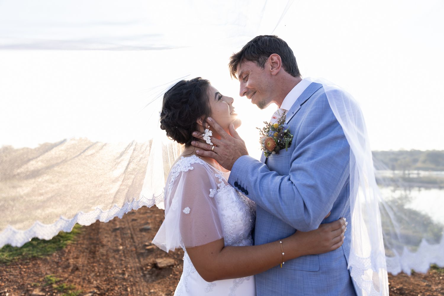A couple embraces lovingly against a waterfront backdrop during their wedding.