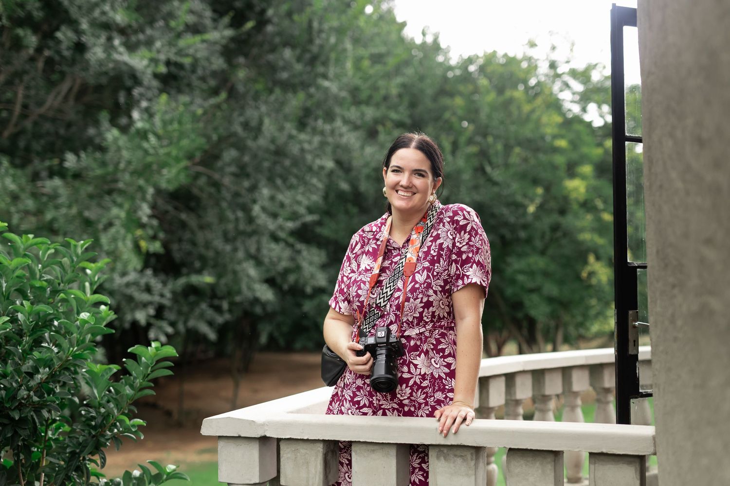 A casual outdoor portrait on a wooden bench surrounded by lush greenery.