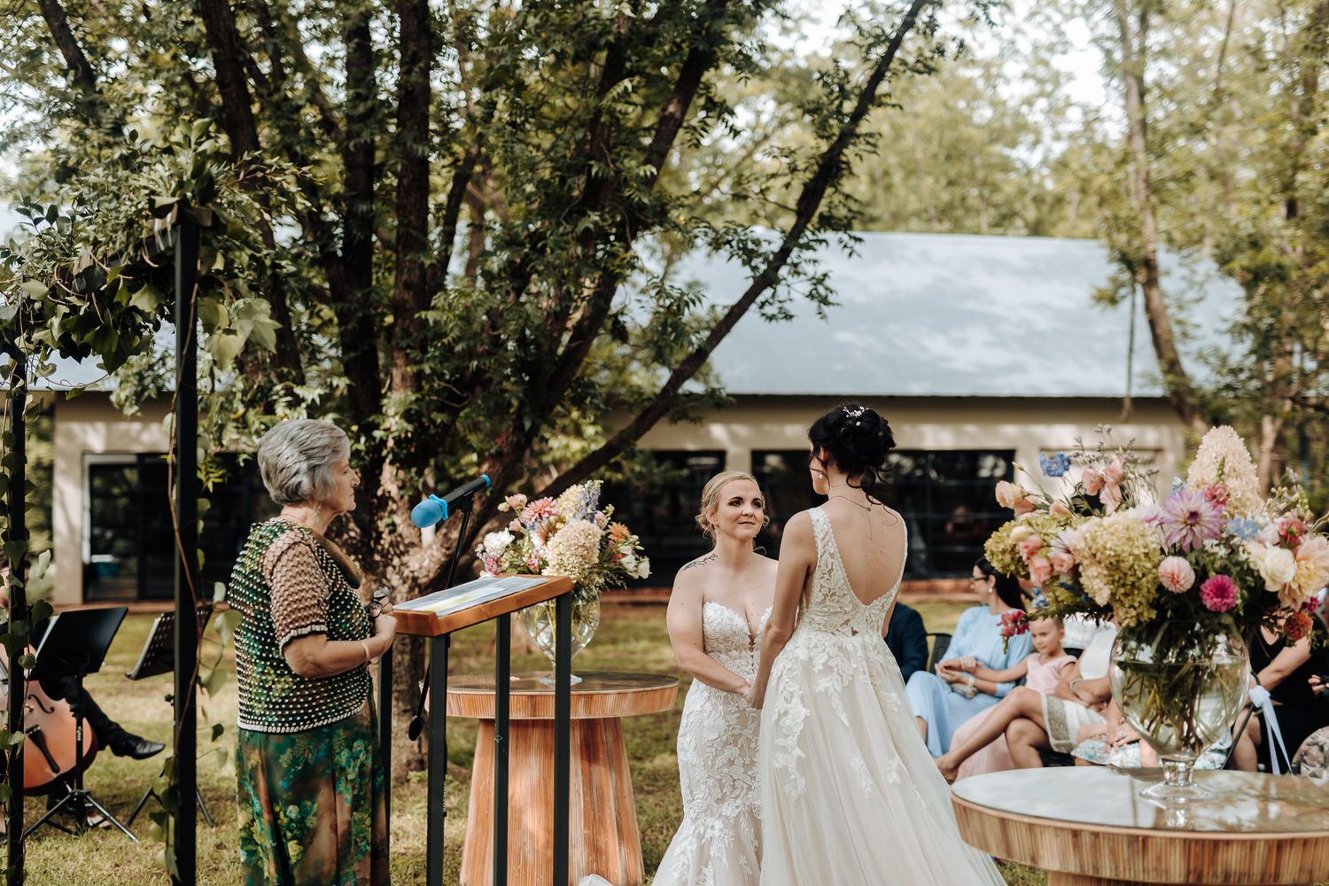 Outdoor wedding celebration with wooden decor and floral arrangements in a garden setting.