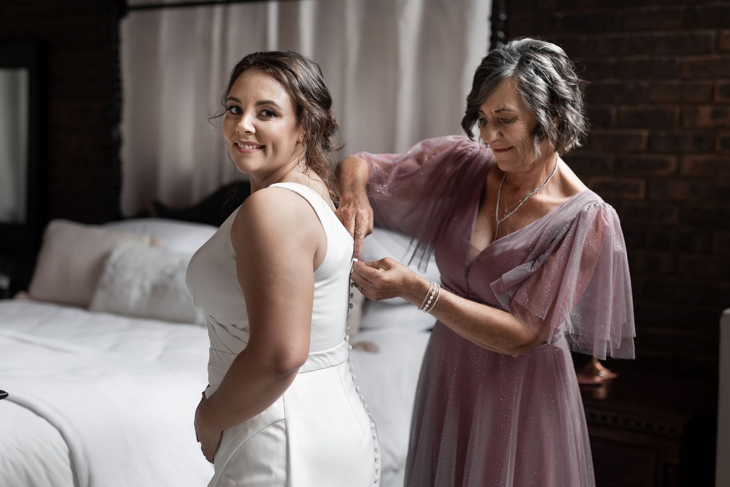 Getting ready scene with white wedding dress being adjusted in bedroom.