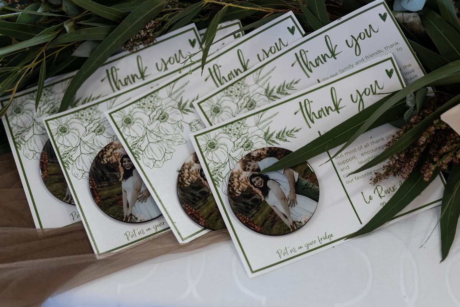 Multiple 'Thank You' wedding cards with photo inserts arranged with eucalyptus leaves.