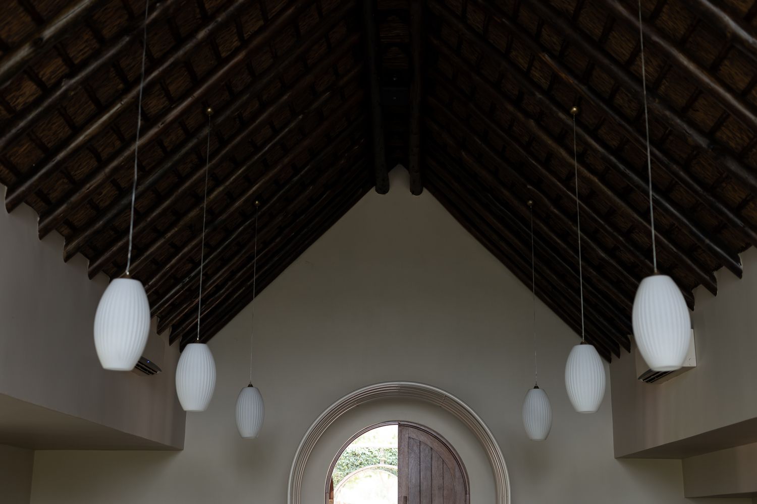 White pendant lights hang from a dark wooden cathedral ceiling in an elegant interior space.
