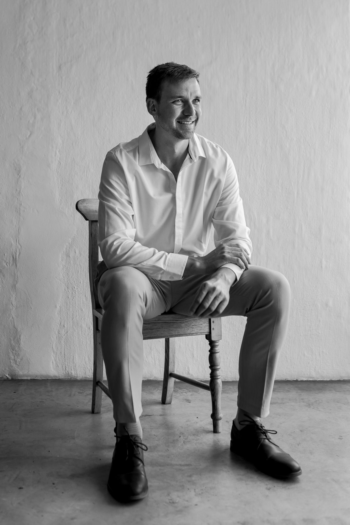 Black and white portrait in minimalist setting with wooden chair.