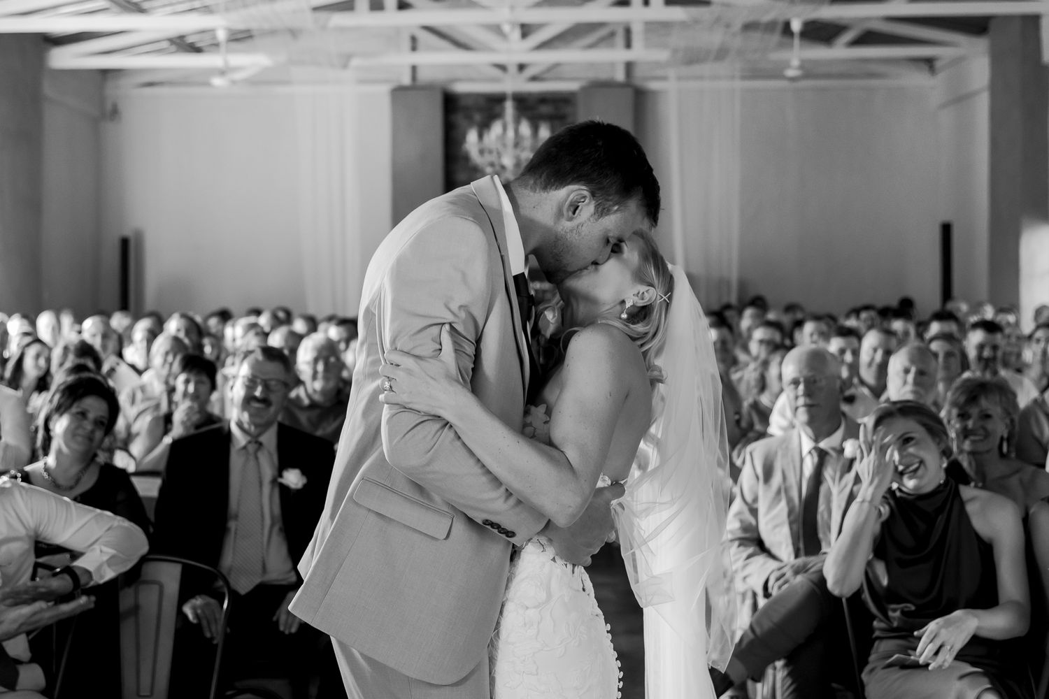 Black and white photo of a couple's intimate first kiss during their wedding ceremony.