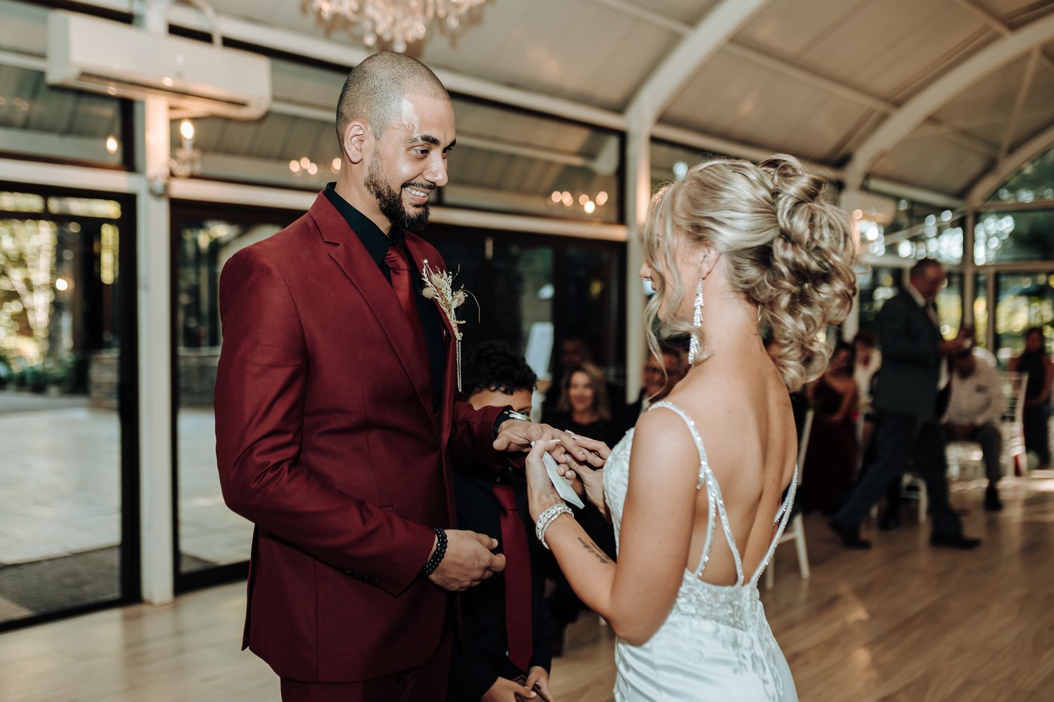Couple exchanges vows during intimate indoor ceremony beneath crystal chandeliers.