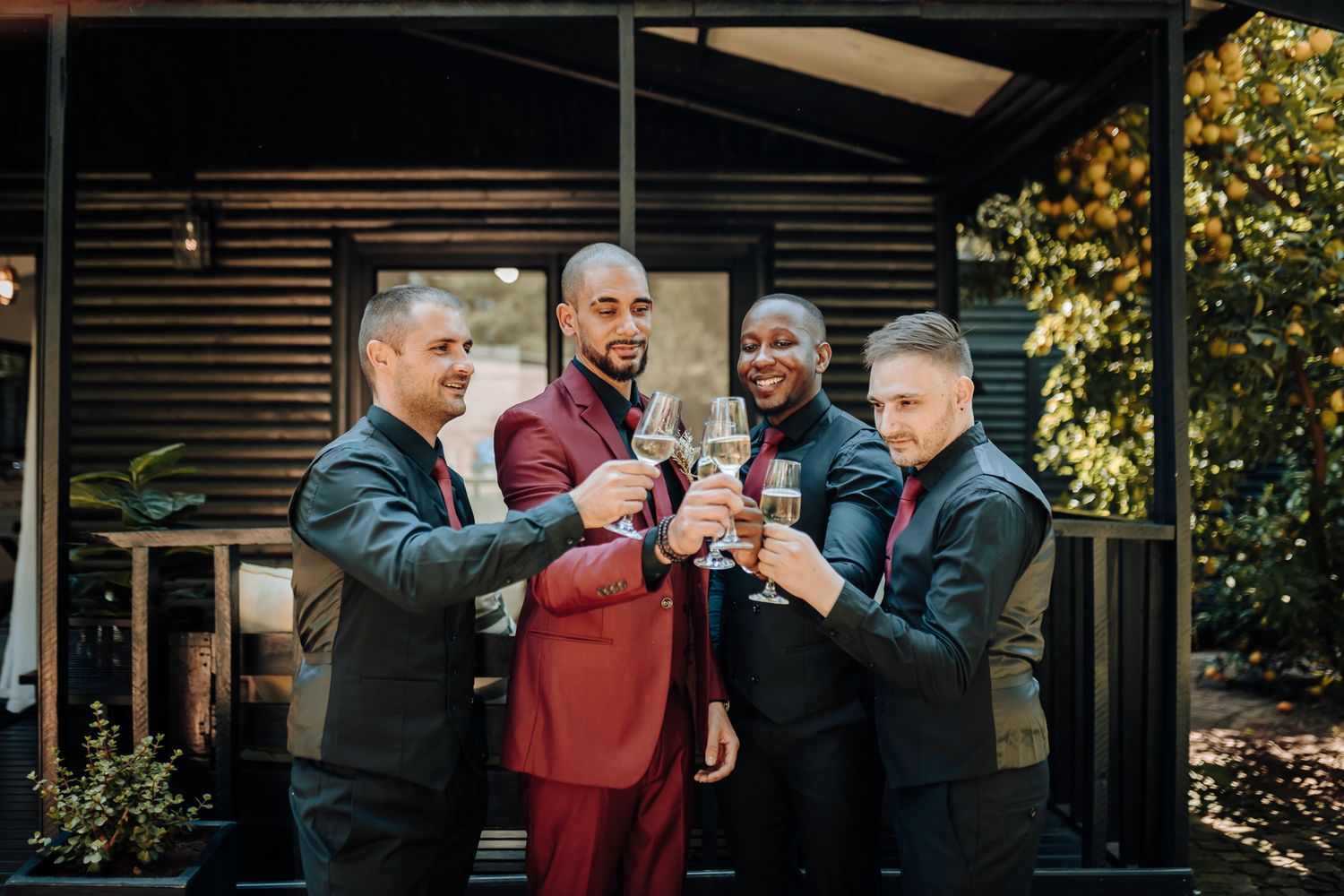 Groomsmen in suits toasting with champagne glasses outdoors.