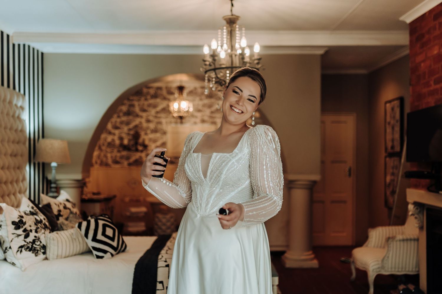 Bride in long sleeve wedding dress checking phone in ornately decorated room.