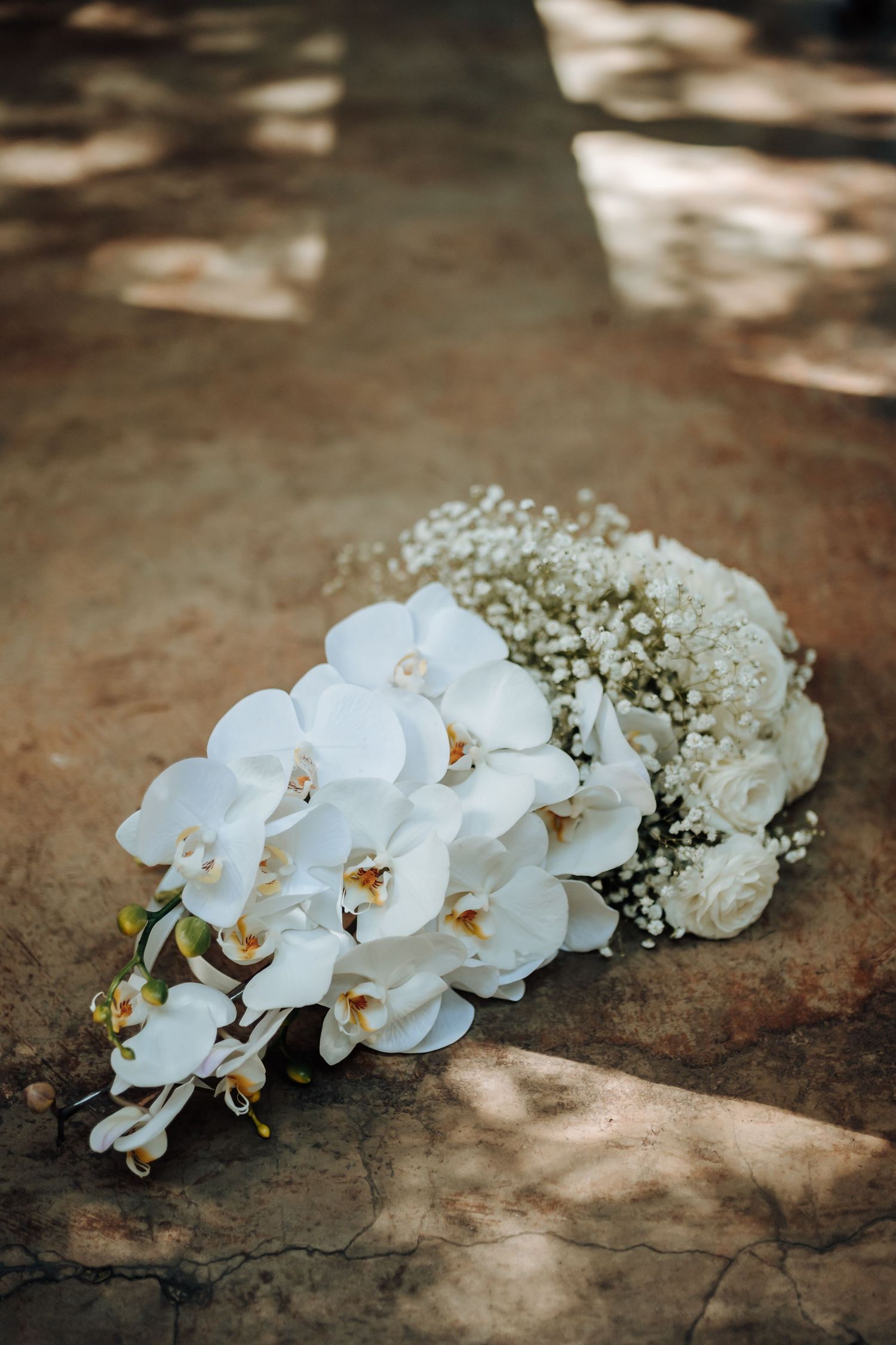 A cascading white orchid and baby's breath bridal bouquet on stone ground.