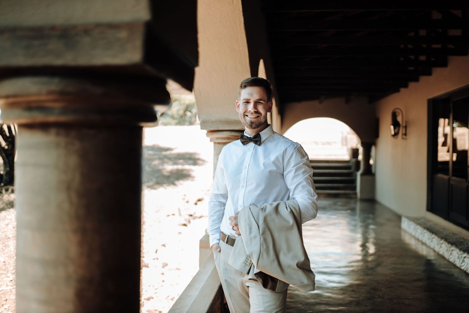 A formal figure in light colored attire walking through an arched outdoor corridor.