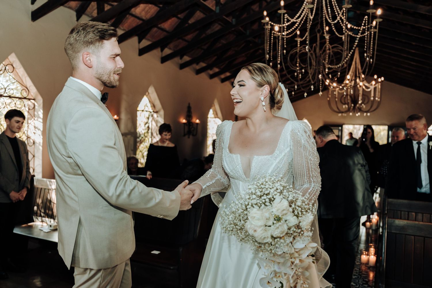 Wedding ceremony in rustic chapel with exposed beams, chandelier and gothic arched windows.