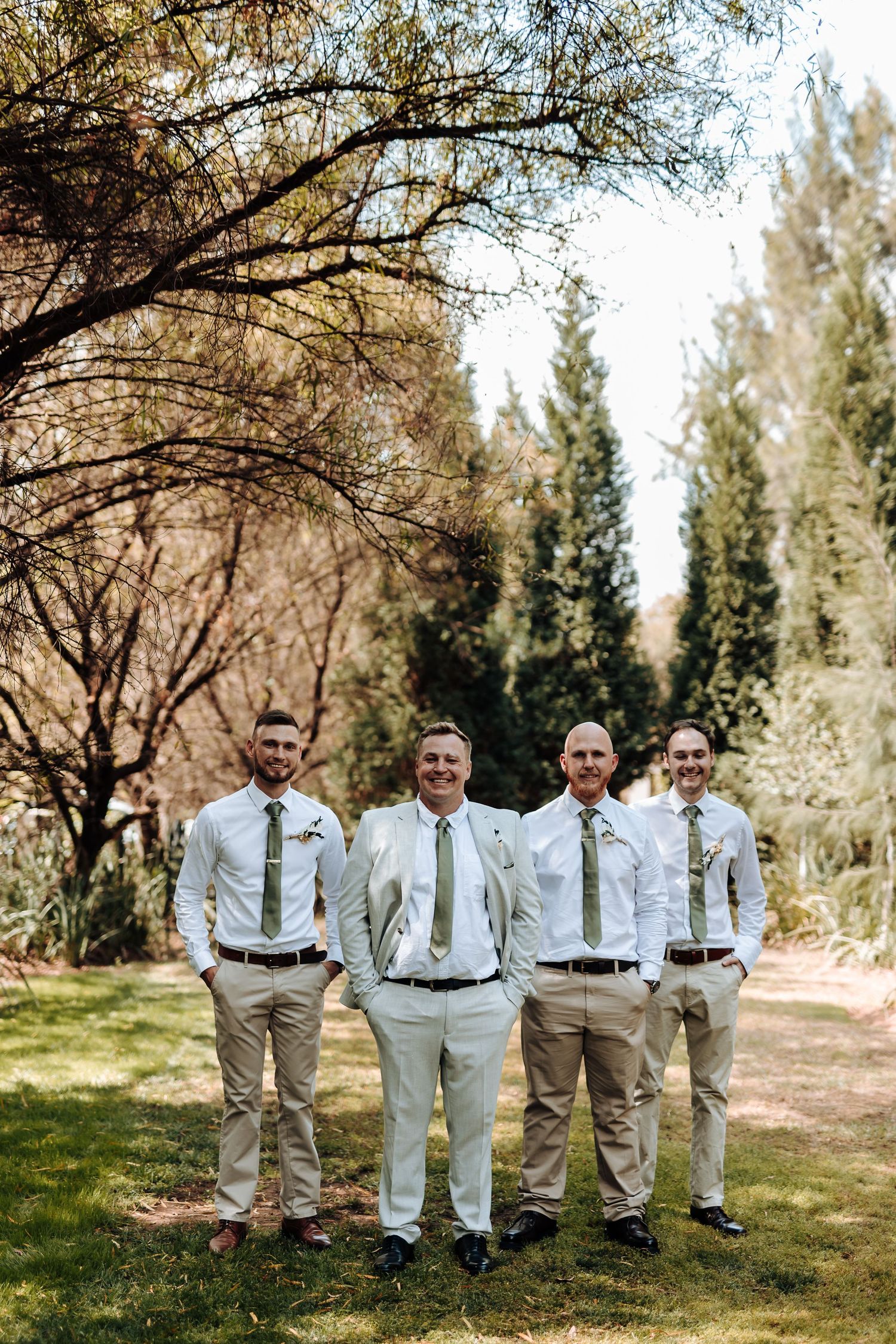 Wedding party in coordinated white and khaki attire poses together on grassy outdoor path.