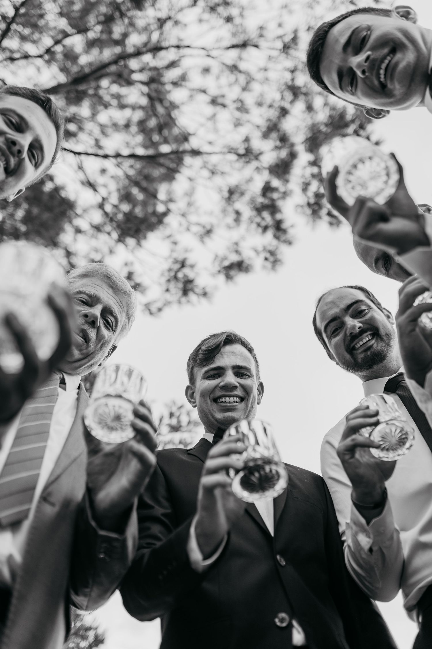 A group toasts with drinks while looking down at the camera in a fun black and white moment.