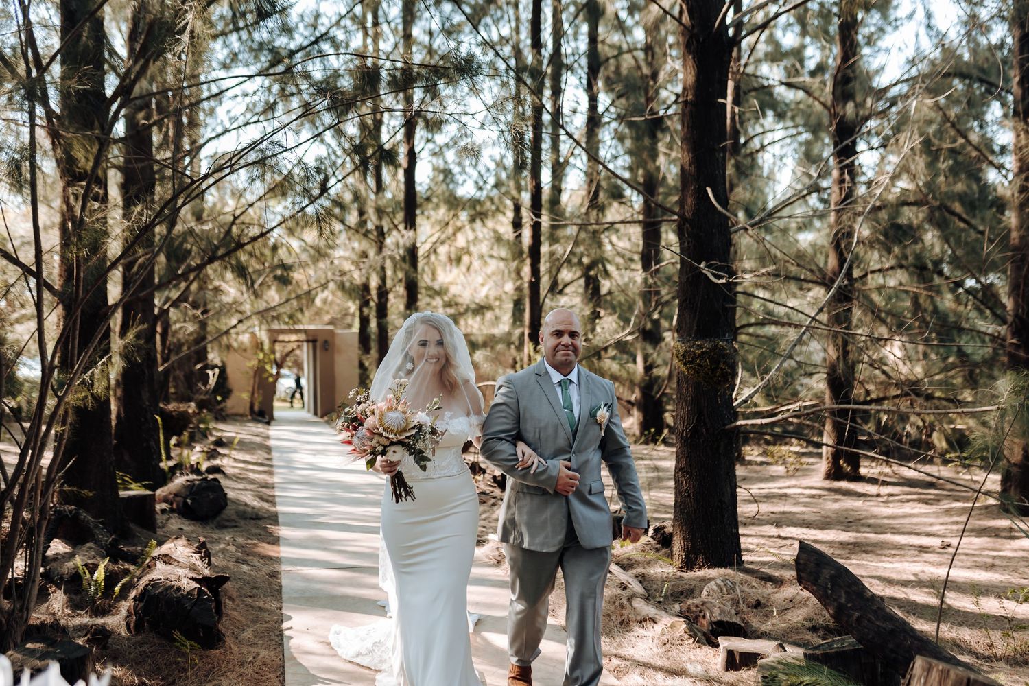 A couple walks down a sunlit forest path after their wedding ceremony.