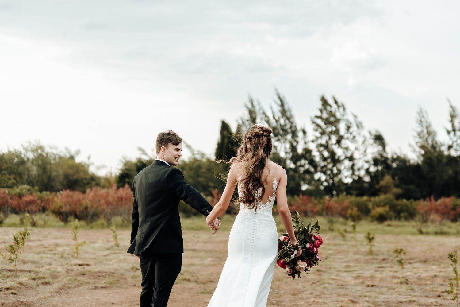 Couple walks hand in hand through rustic field during wedding photoshoot.