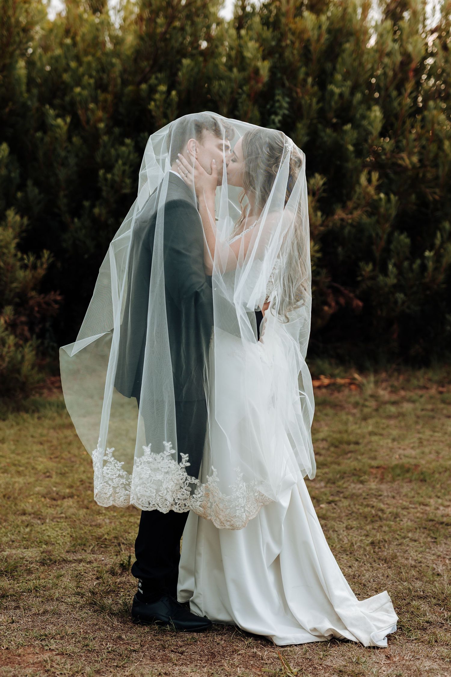 Romantic moment under bride's lace veil during outdoor wedding portraits.