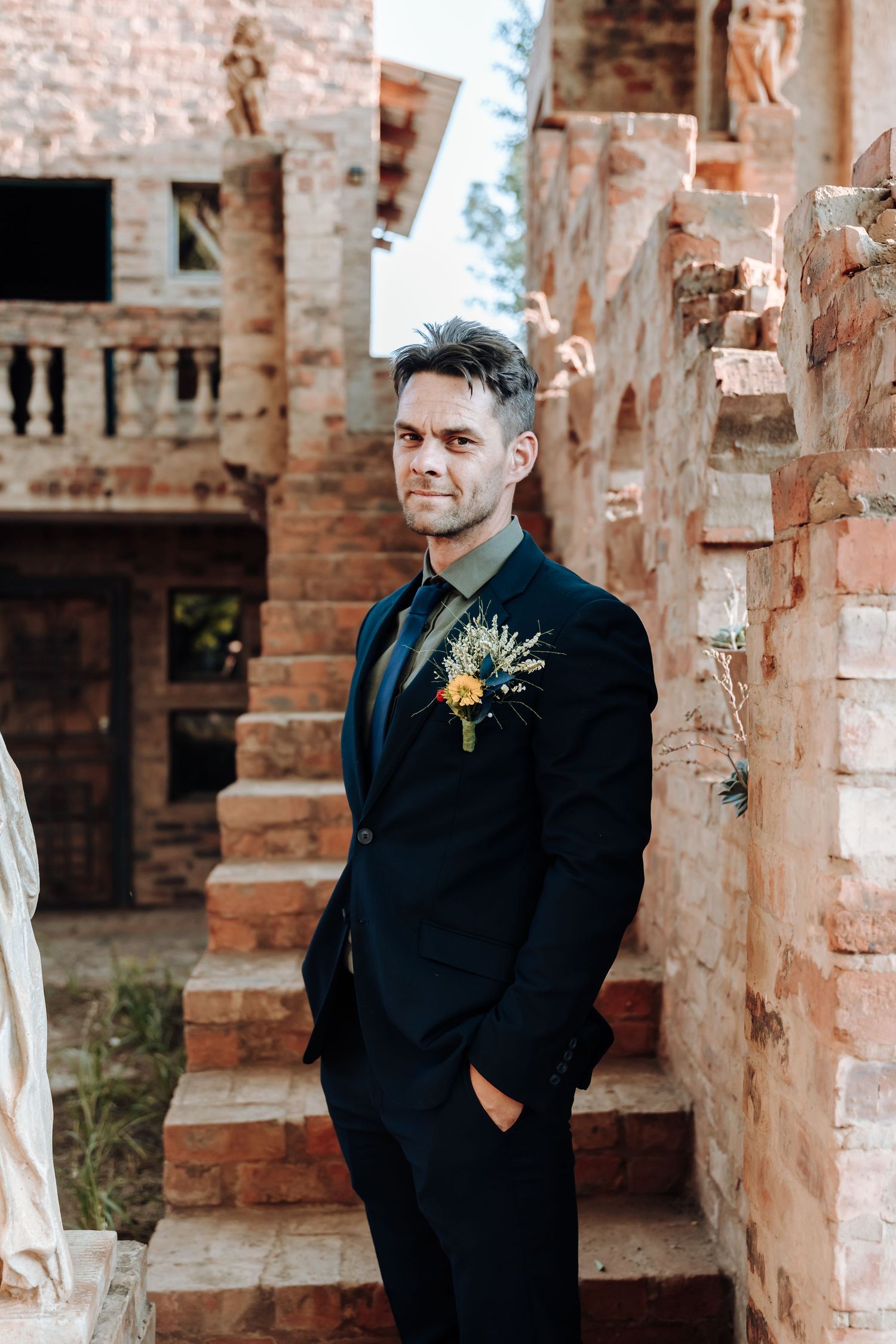 Groom in classic black suit poses on rustic stone staircase with boutonniere.