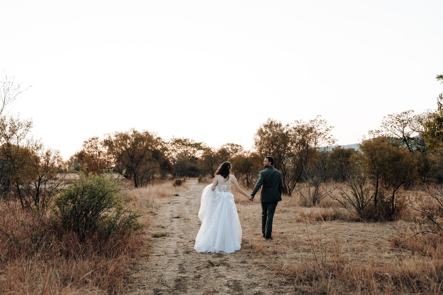 Newlyweds walk down a dirt path together during golden hour.