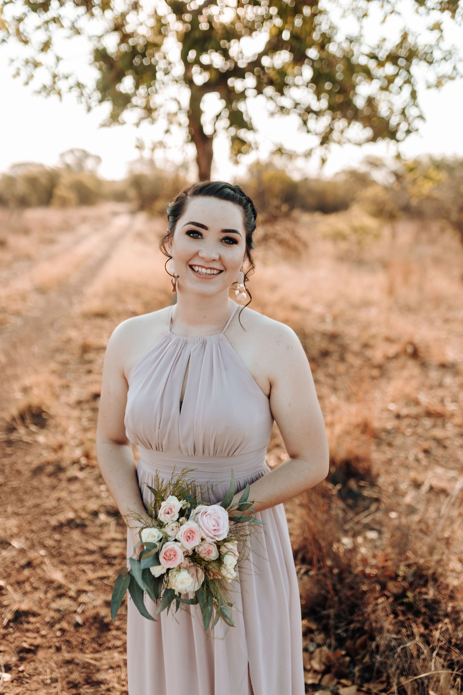 Bridesmaid in elegant blush halter dress holding pink and white bouquet outdoors.