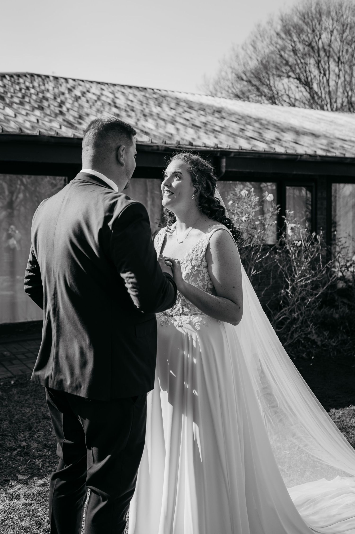 Black and white photo of a tender moment between newlyweds, with the bride in a flowing gown and veil outdoors.