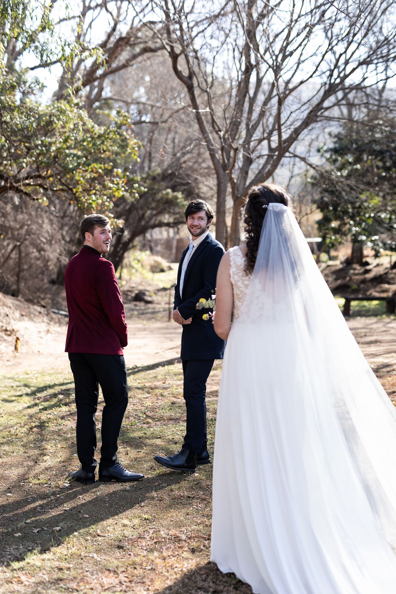 Outdoor winter wedding scene with white bridal gown flowing in the breeze as three people gather for ceremony in nature.