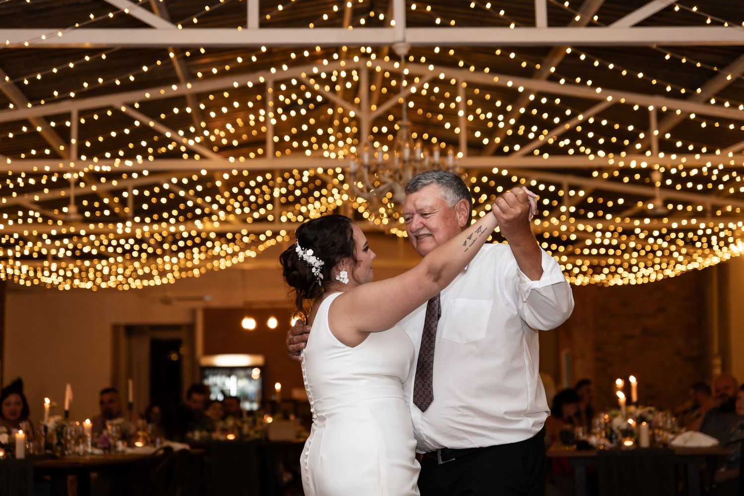 A couple shares their first dance under a canopy of glowing string lights.