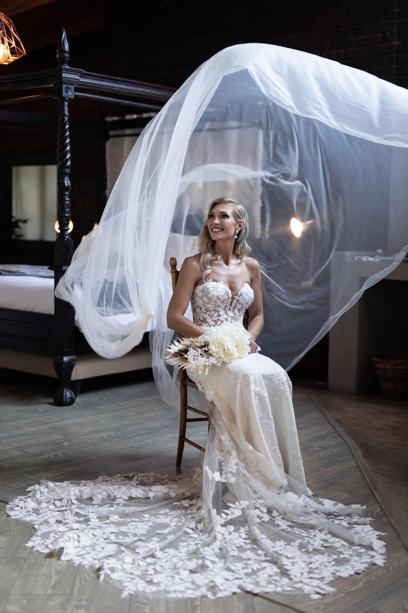 Dramatic bridal portrait with flowing veil and lace gown in rustic indoor setting.