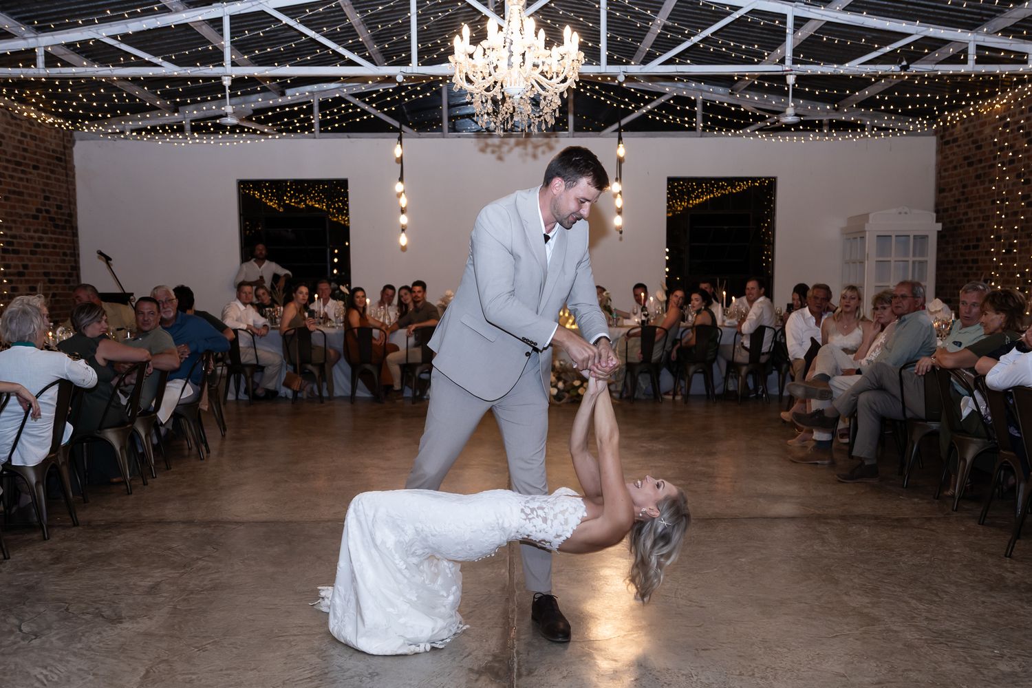 Wedding couple performing fun dance moves on reception floor under string lights.
