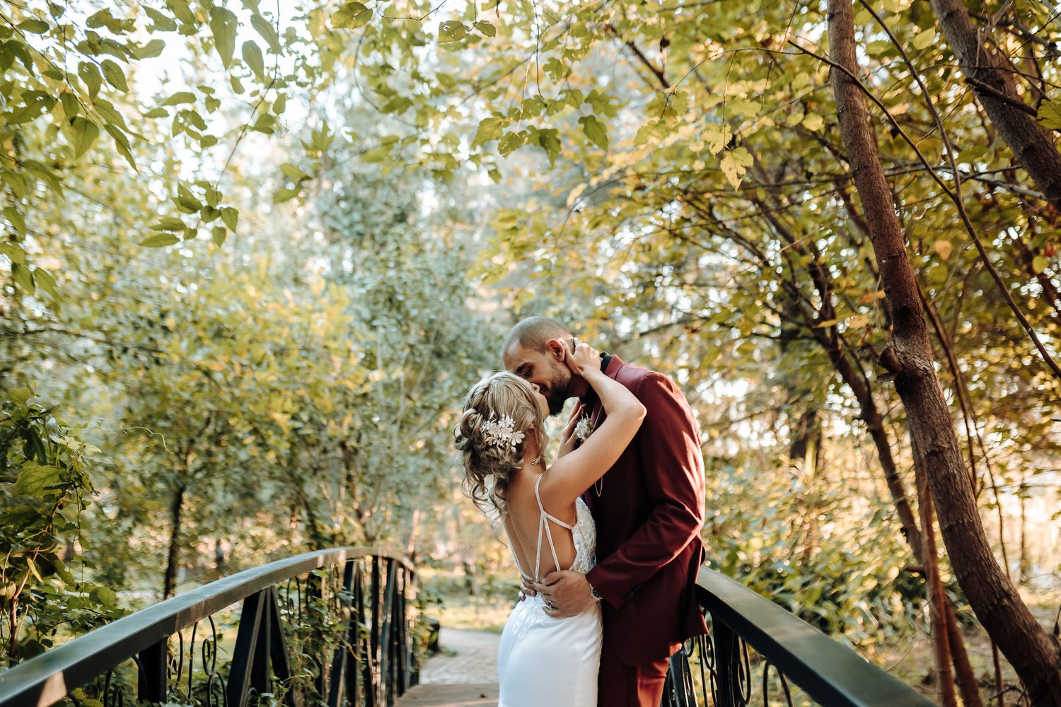 Romantic embrace between newlyweds on a bridge surrounded by autumn trees.