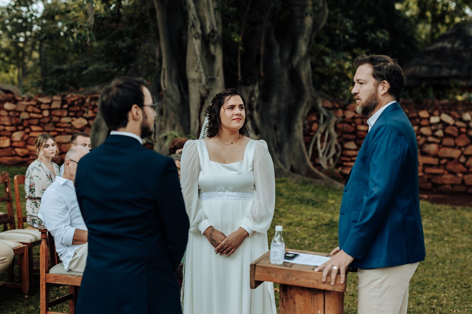 An intimate outdoor wedding ceremony with a wooden podium and stone wall backdrop.