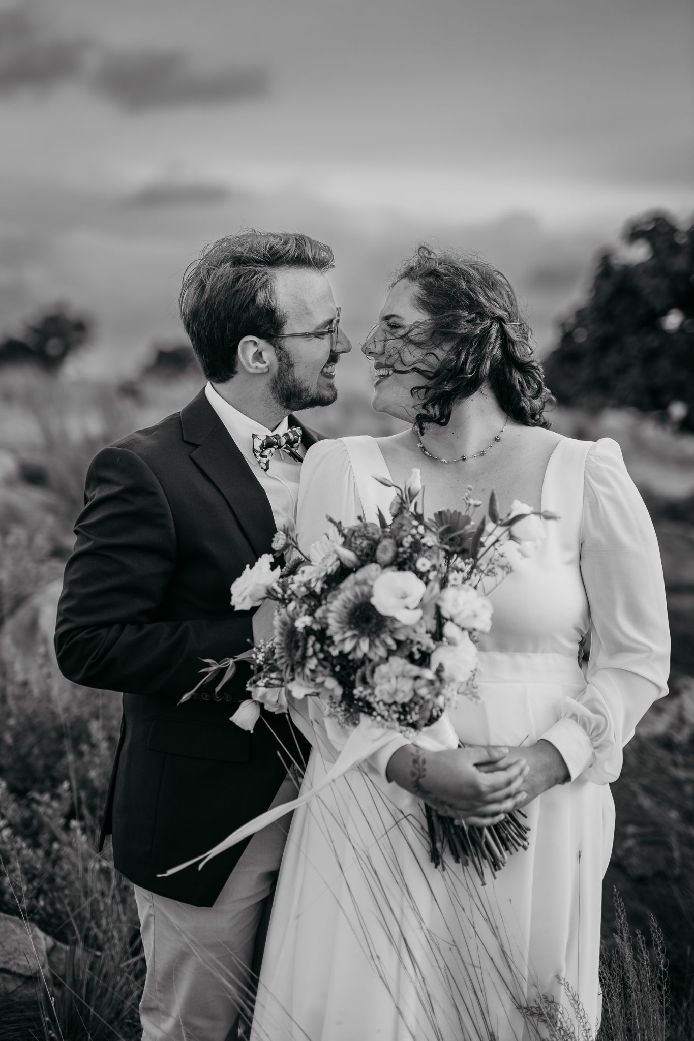 Black and white portrait of couple sharing intimate moment with floral bouquet.