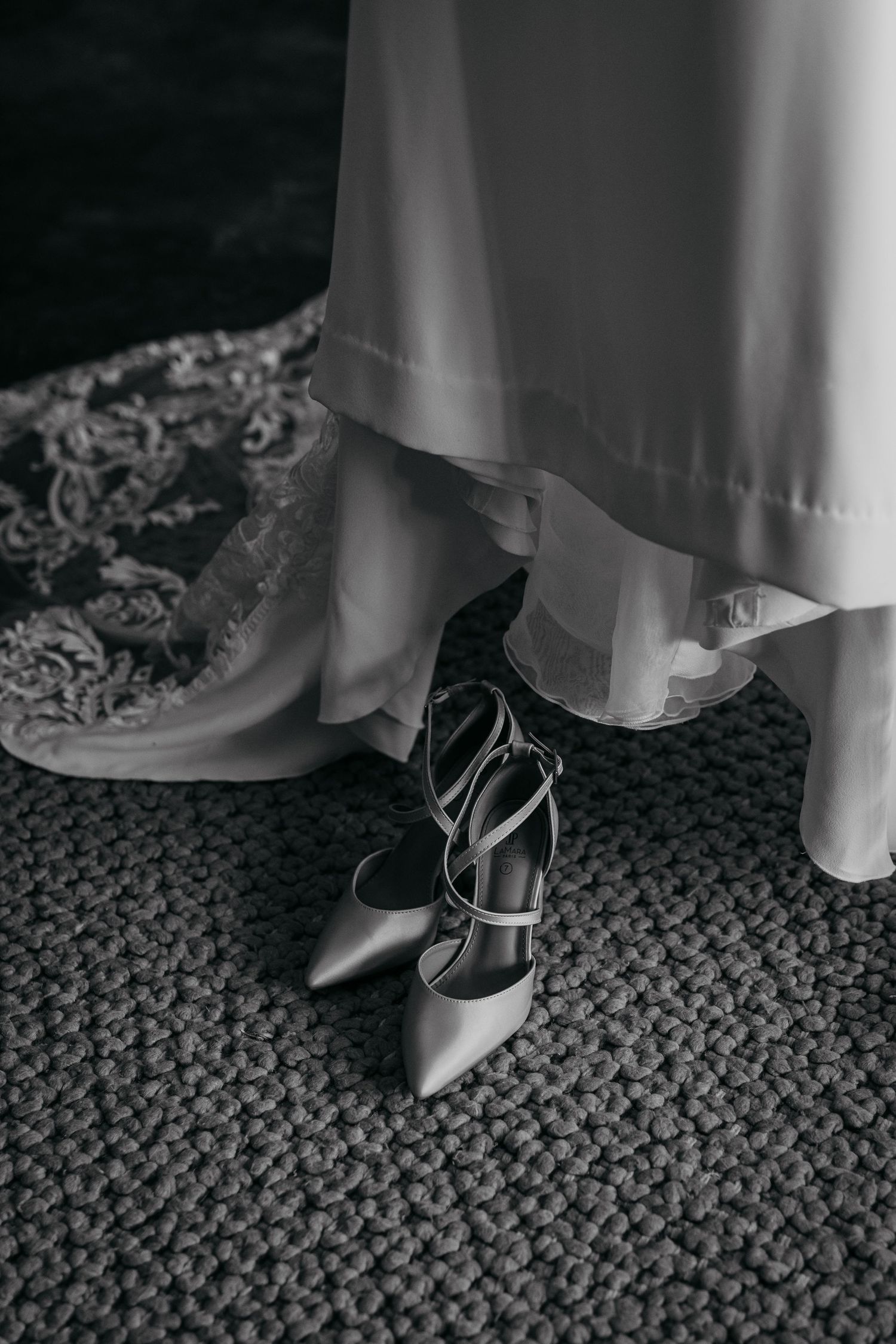 Black and white detail shot of elegant bridal shoes with lace-up straps on textured carpet.