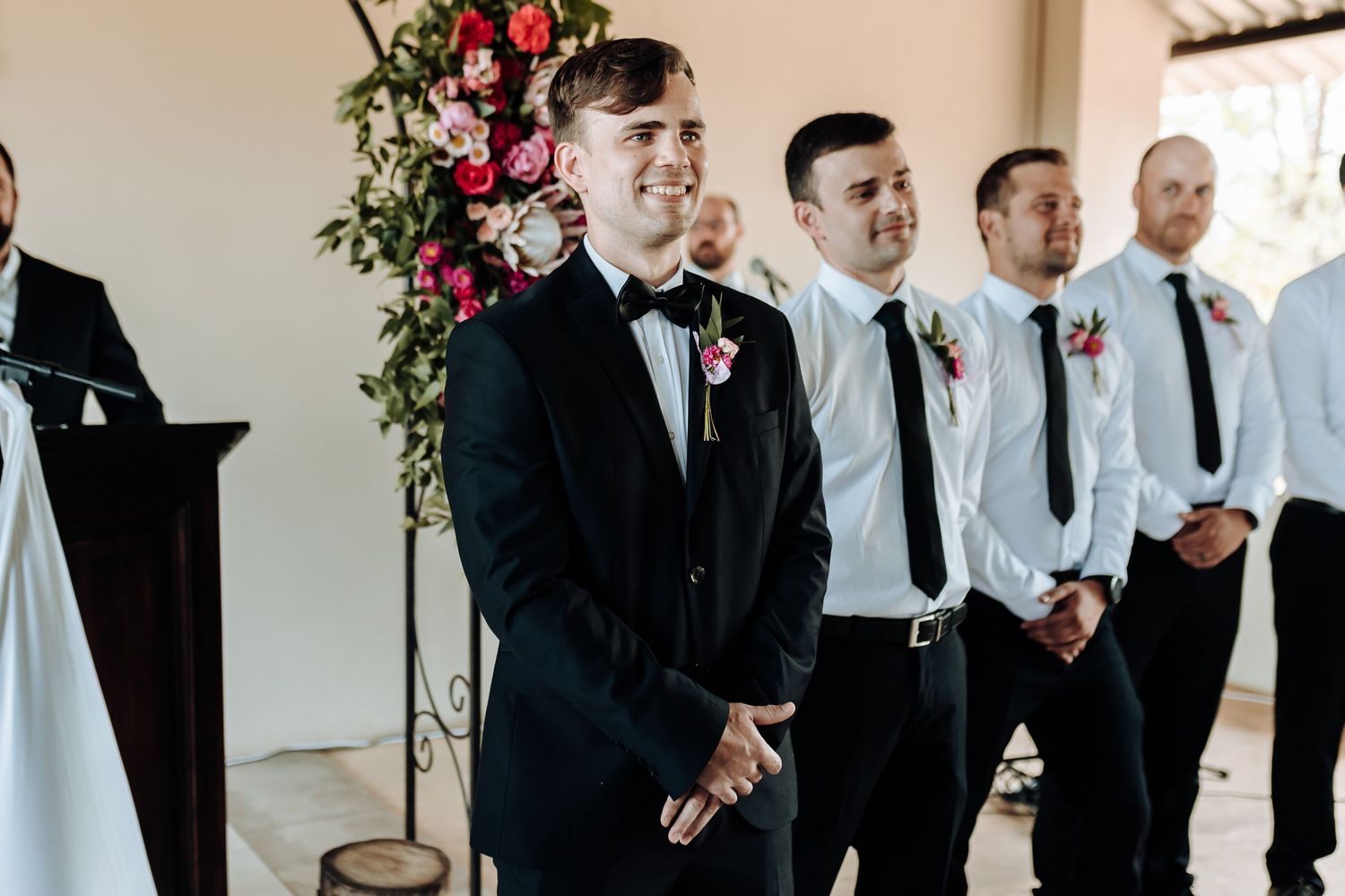Groomsmen stand at altar during ceremony with floral arch backdrop.