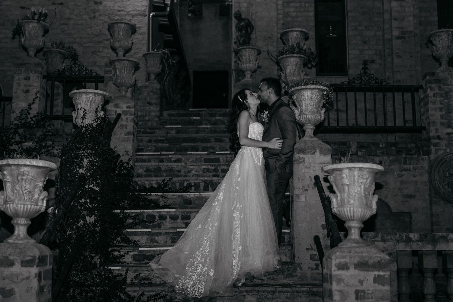 Romantic black and white wedding portrait of couple on stone steps with decorative urns.