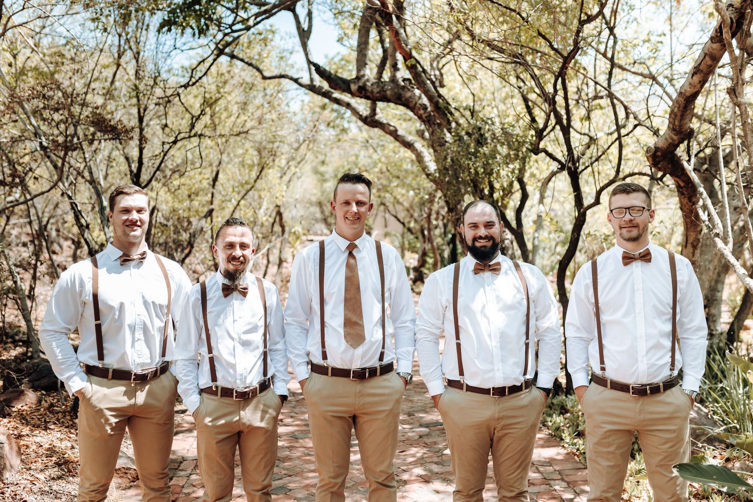 Wedding party in white shirts and suspenders posing together on a nature path.