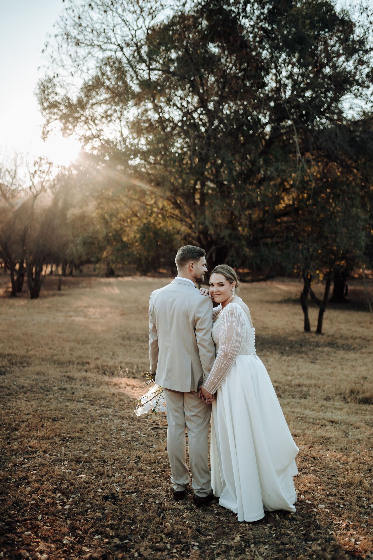 Sunset wedding portrait captures couple holding hands in a rustic woodland setting.