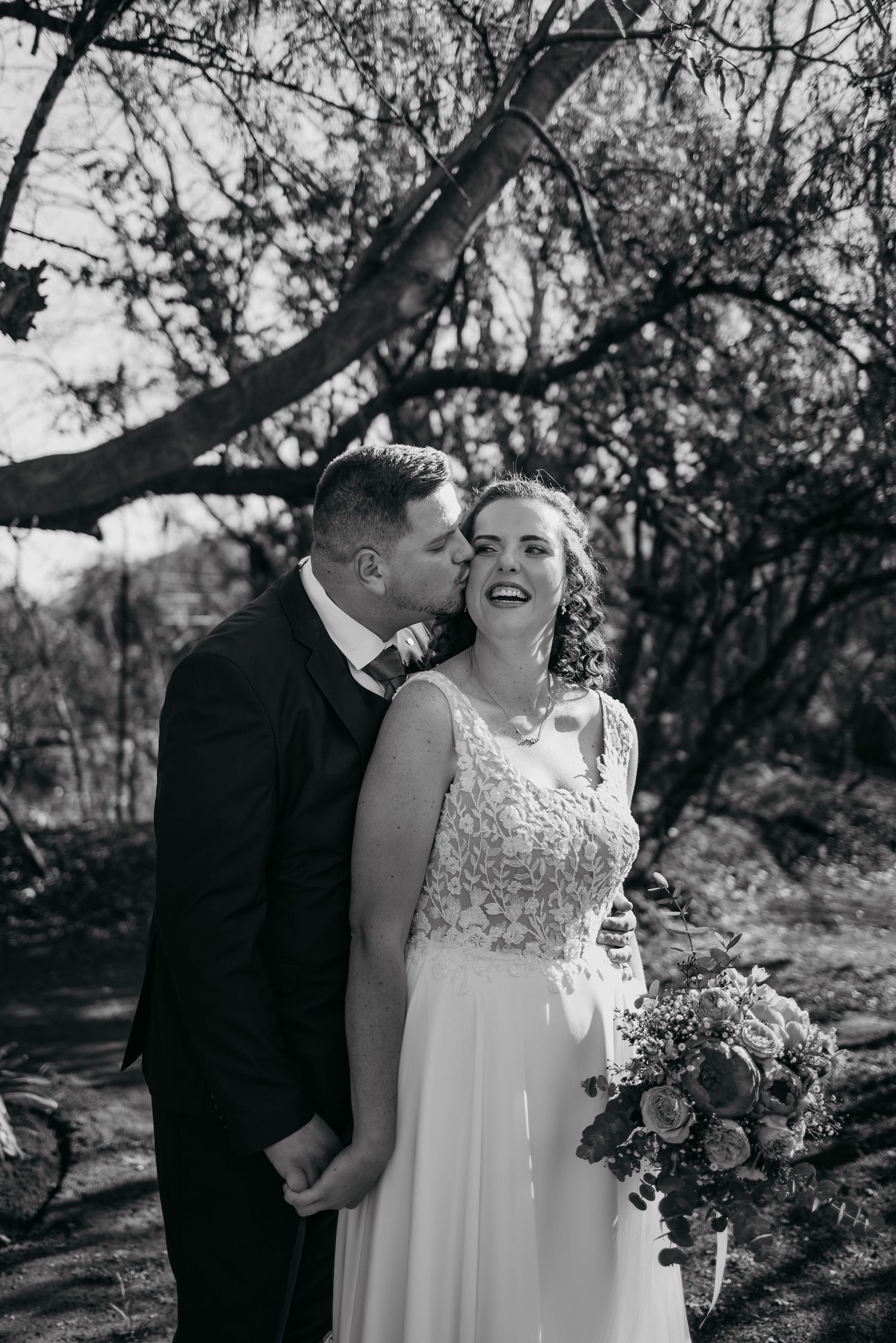 A couple shares joyful moments during their outdoor wedding photoshoot in a natural park setting.