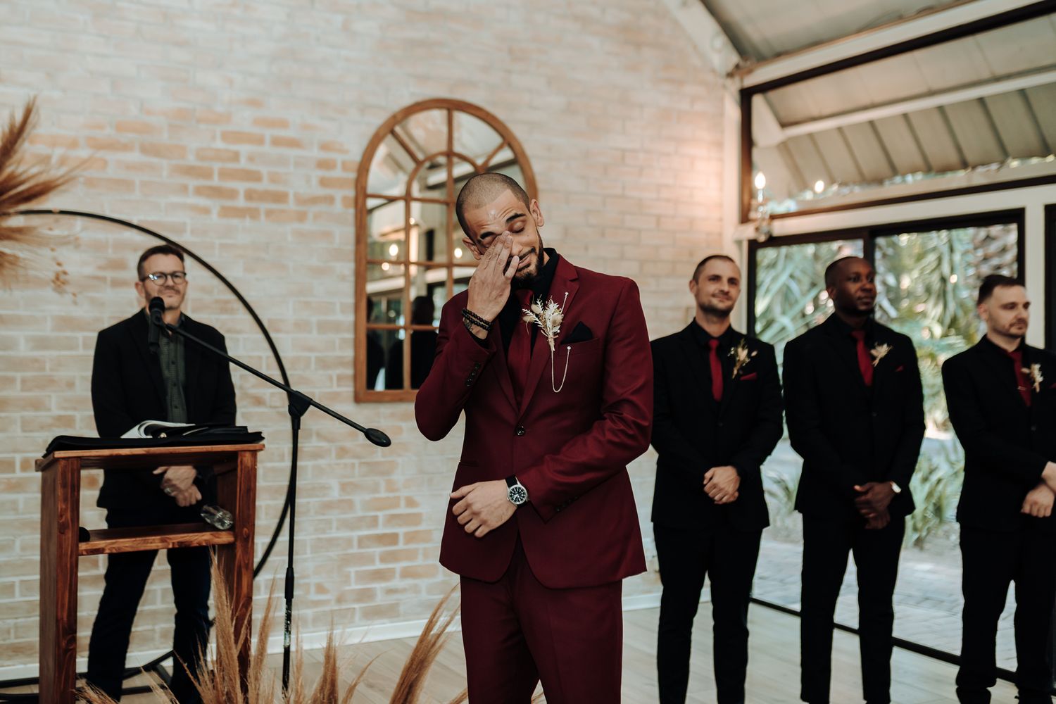 Wedding band performs in a brick-walled venue with singer in burgundy suit and musicians in dark attire.