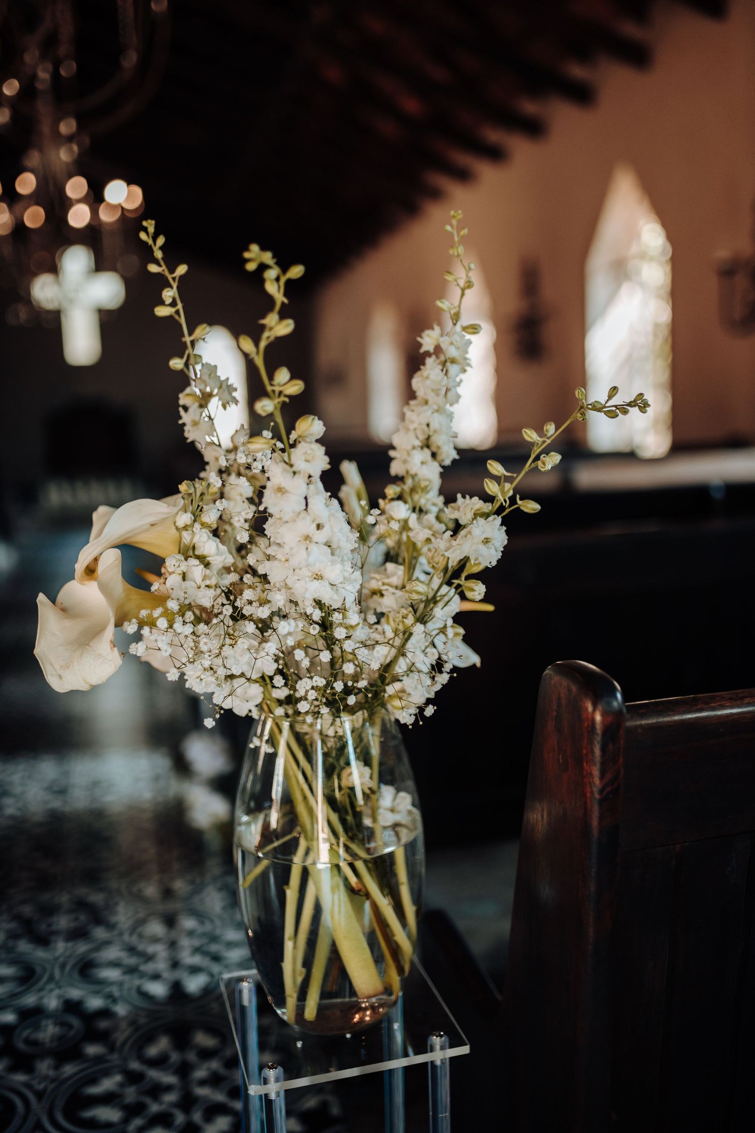 White floral arrangement with delicate baby's breath and calla lilies in glass vase against church background.