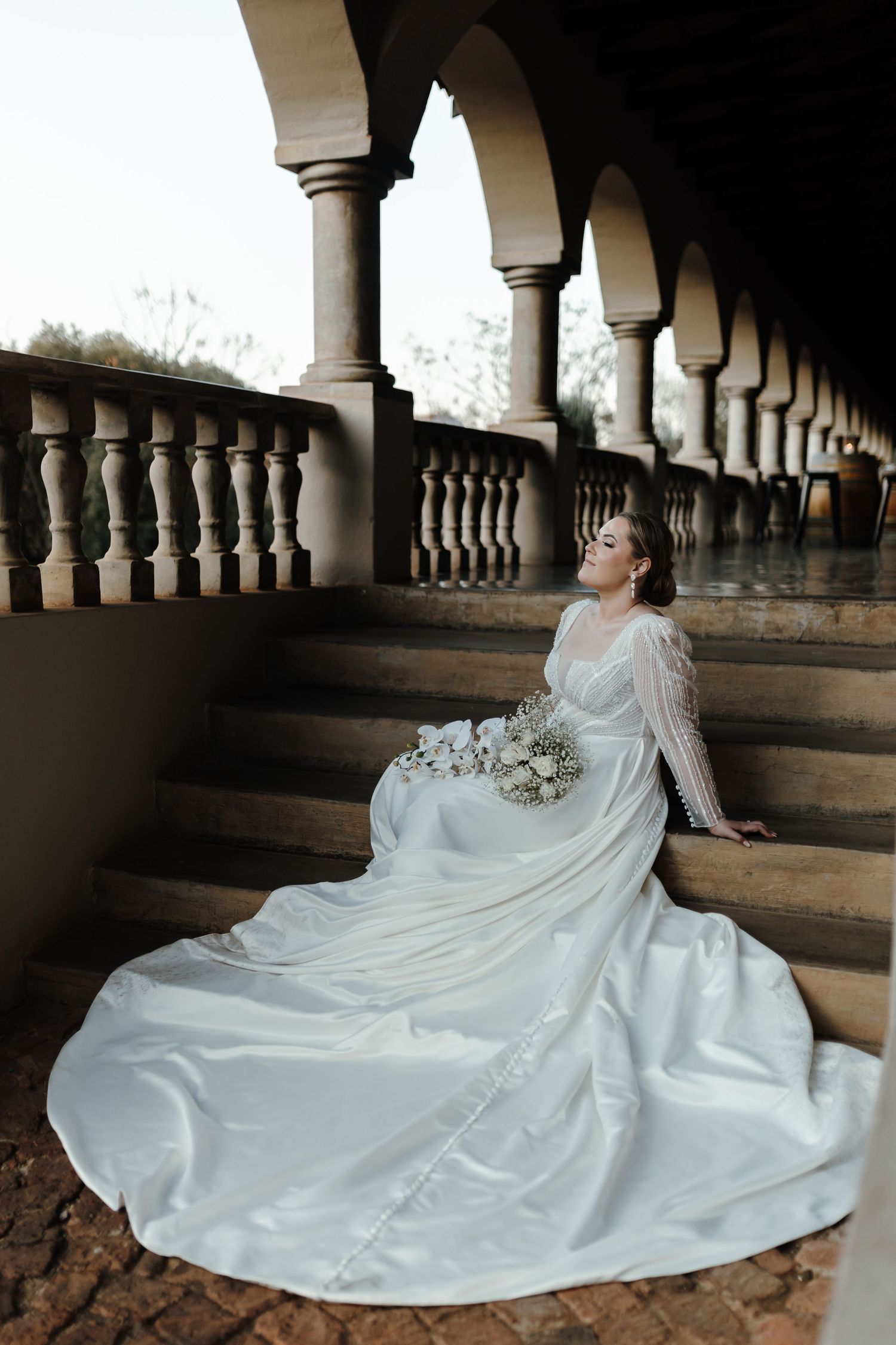 Elegant wedding gown with long train photographed against architectural columns and stone steps.
