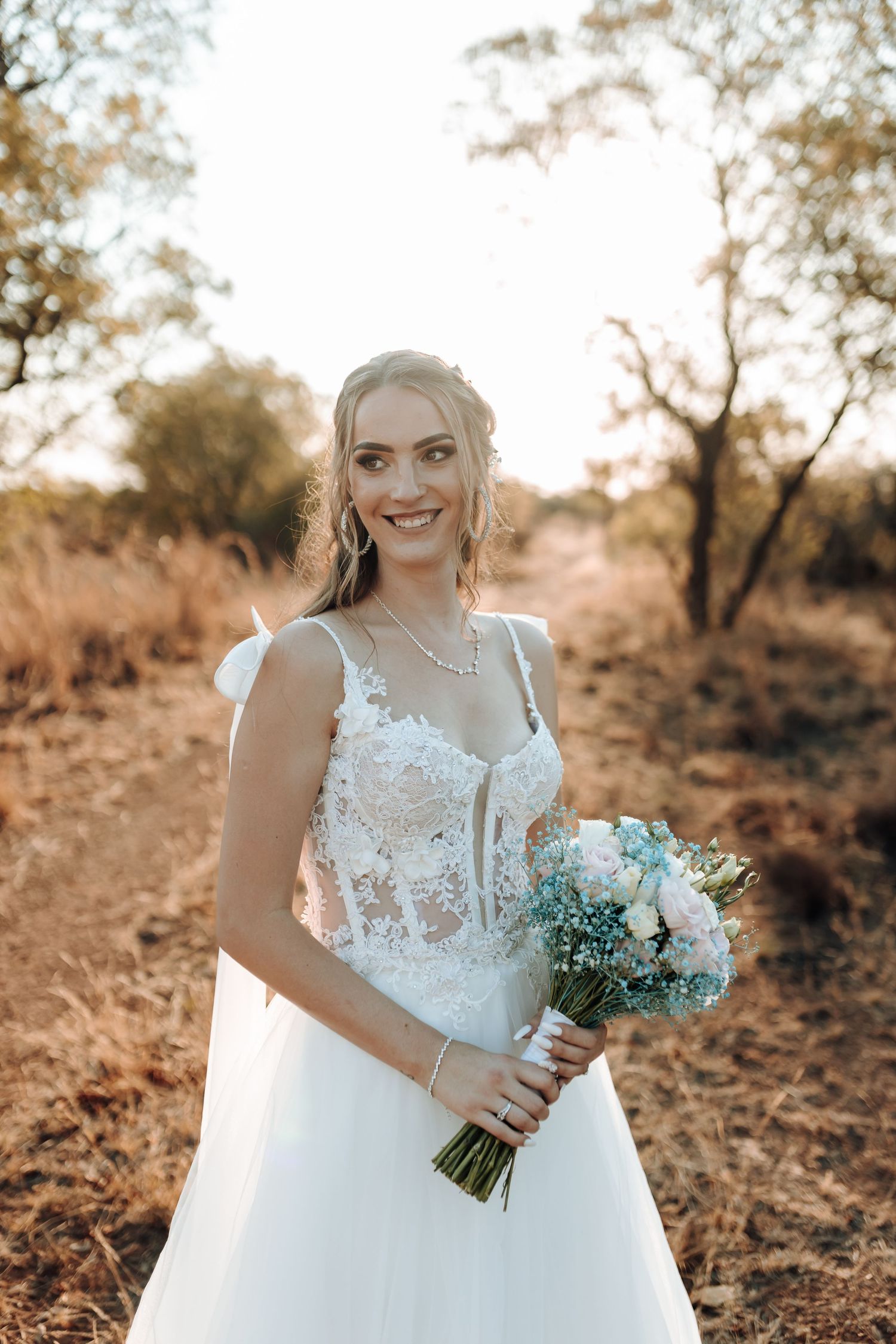 Bride with pastel bouquet poses on nature trail during golden hour.