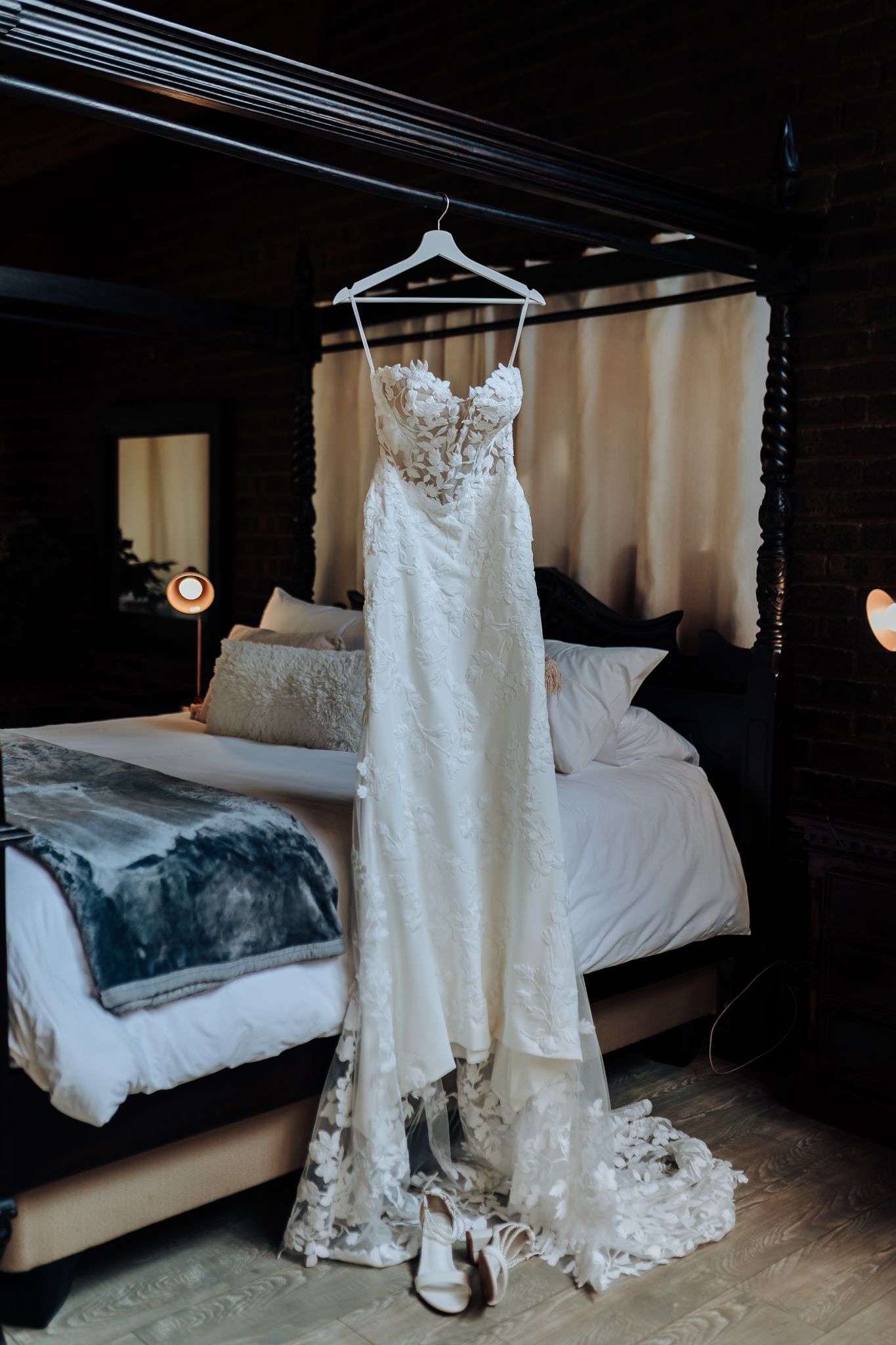 Lace wedding dress with sweetheart neckline hanging on display in a rustic bedroom setting.