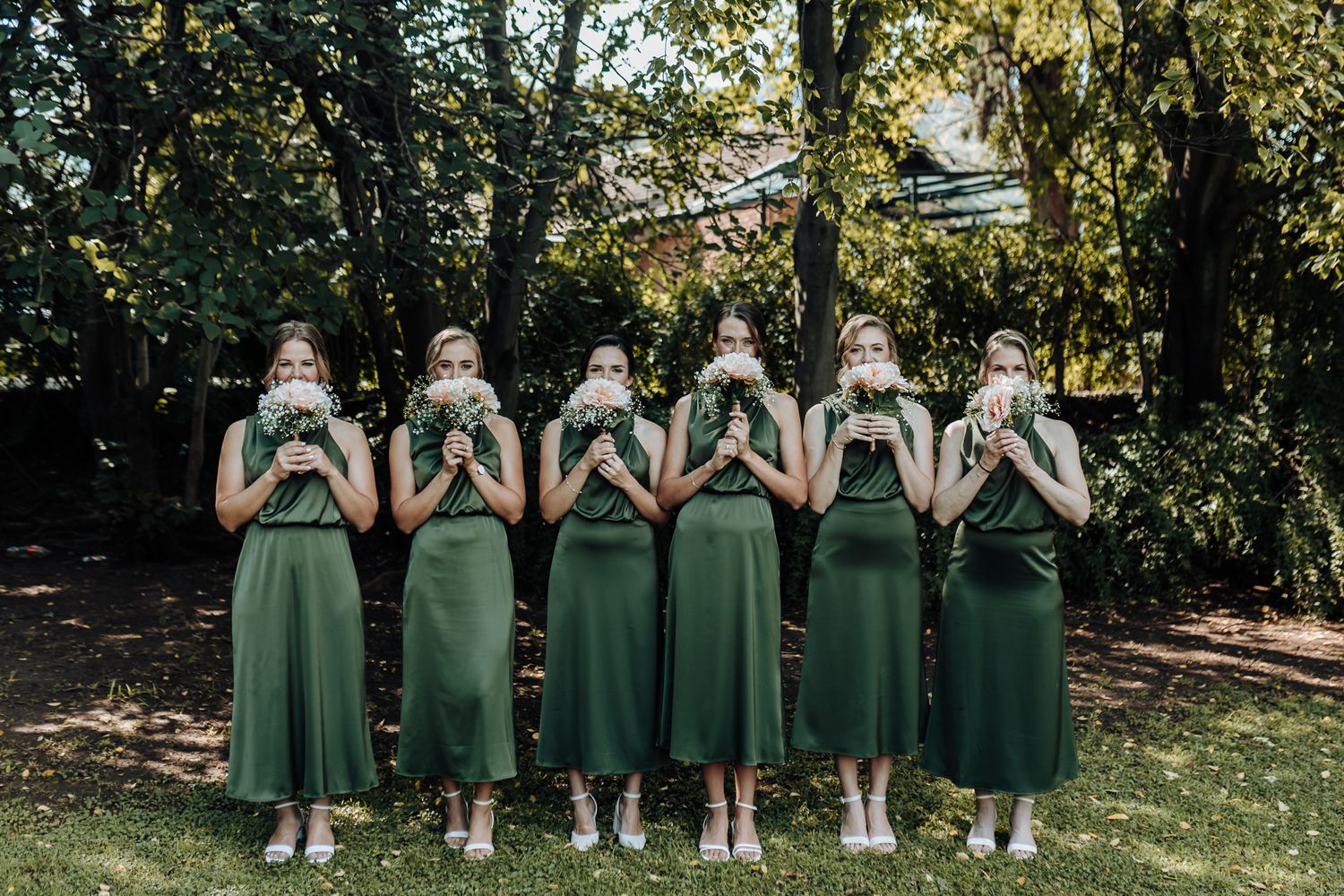 Bridesmaids in green dresses pose facing away showing identical backs of dresses.