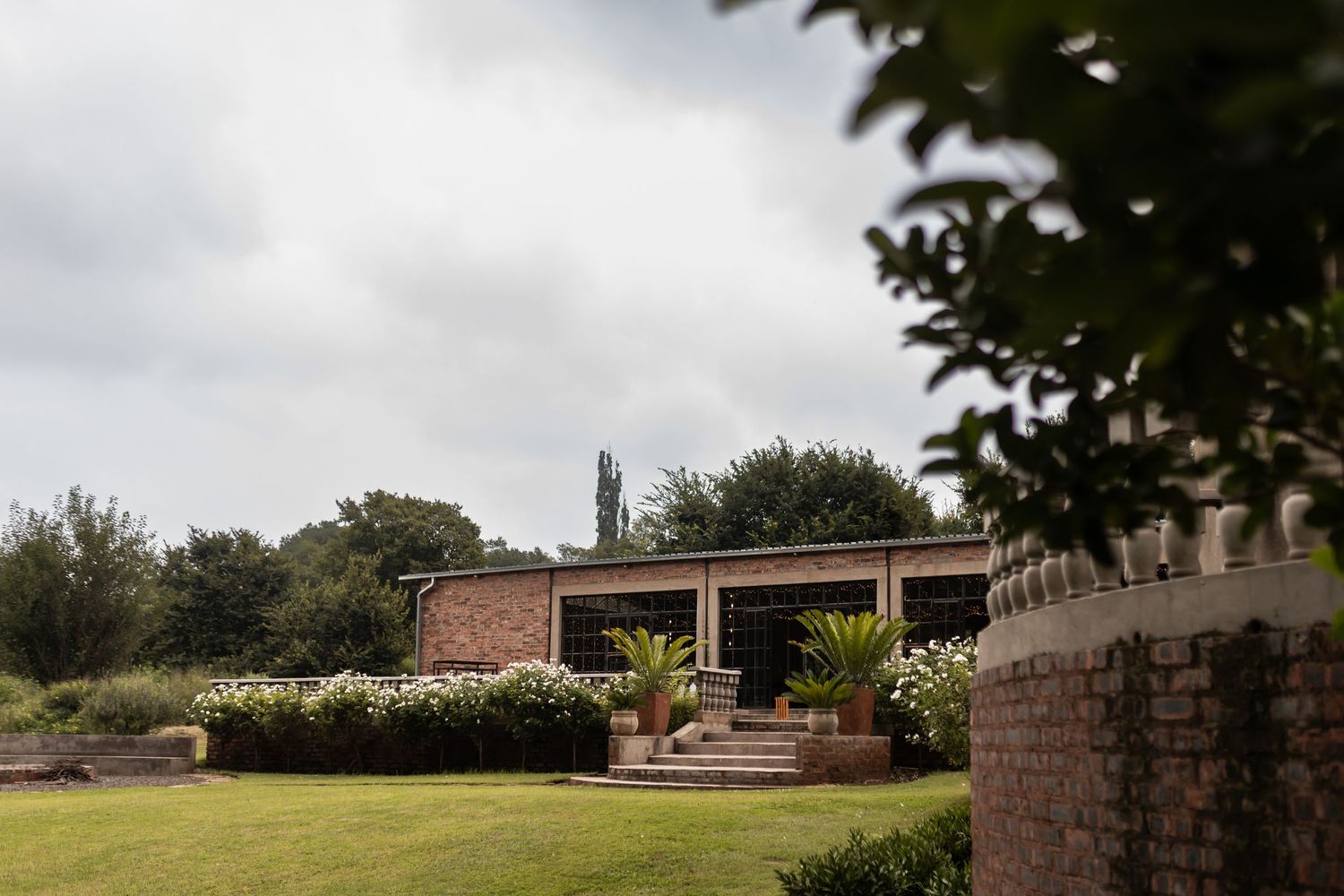 Modern brick building with landscaped garden grounds and cloudy sky backdrop.